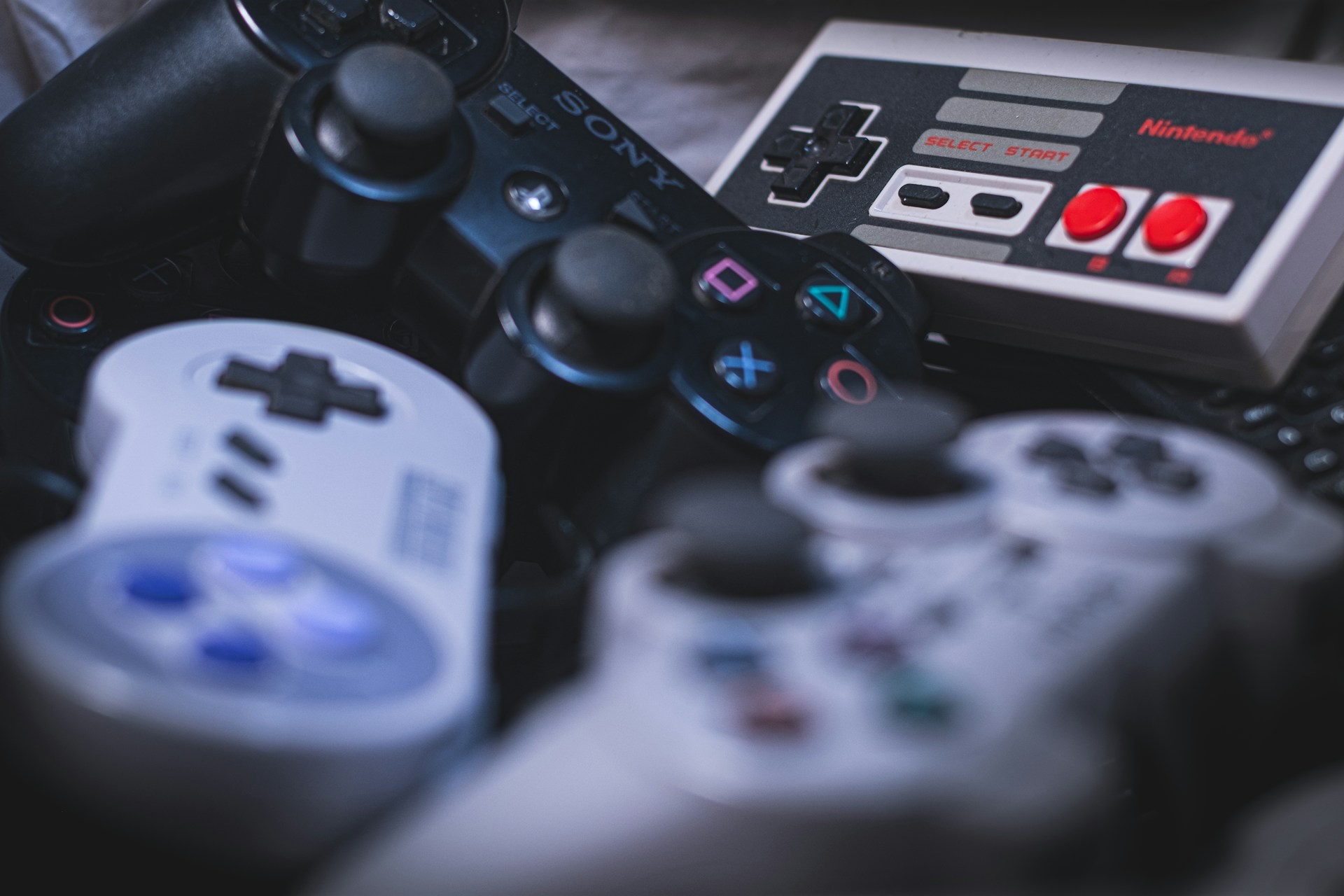 controllers from different consoles stacked on a table to represent the impact Adam's Venture has had on gaming Image source: https://unsplash.com/photos/white-sony-ps-4-game-controller-gSstgCAgd3U