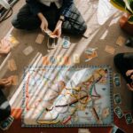 four people sitting on the floor playing strategy board games on a map-like board Image source: https://www.pexels.com/photo/person-in-black-shirt-and-black-pants-sitting-on-brown-and-blue-rug-4691555/