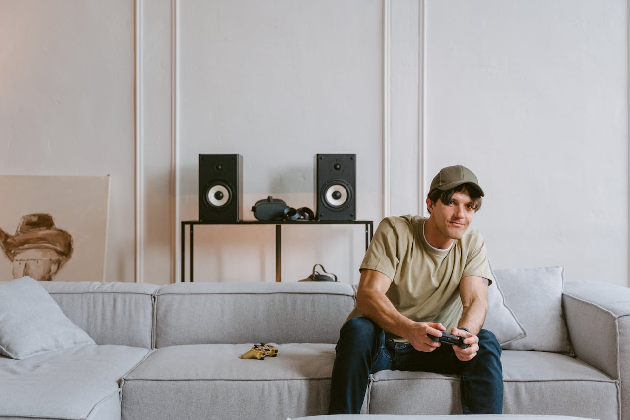 a man sitting in a bright room on a couch holding a Playstation 5 controller while playing Doom: The Dark Ages