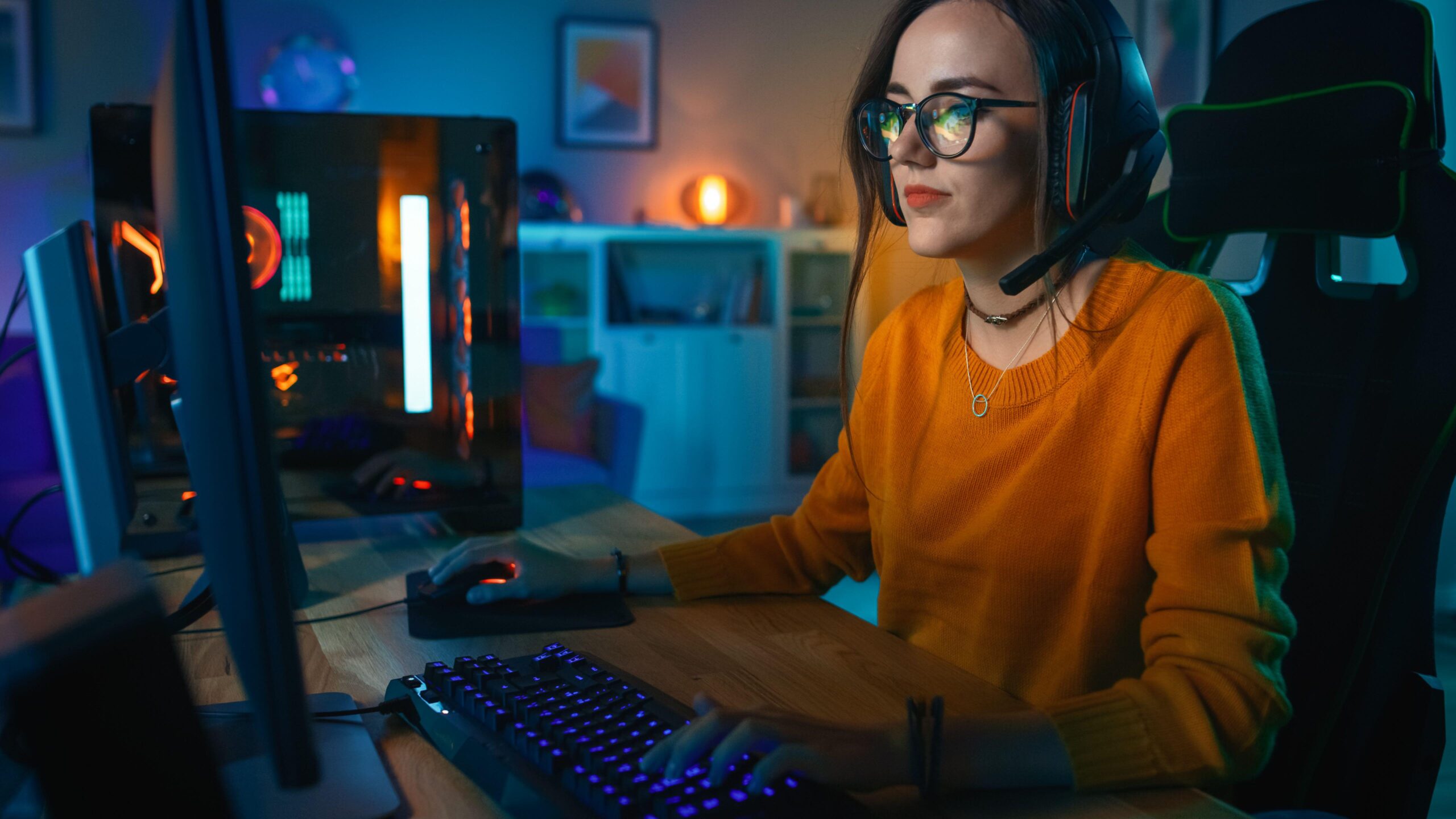 a woman playing Manor Lords on her PC in a dimly lit room