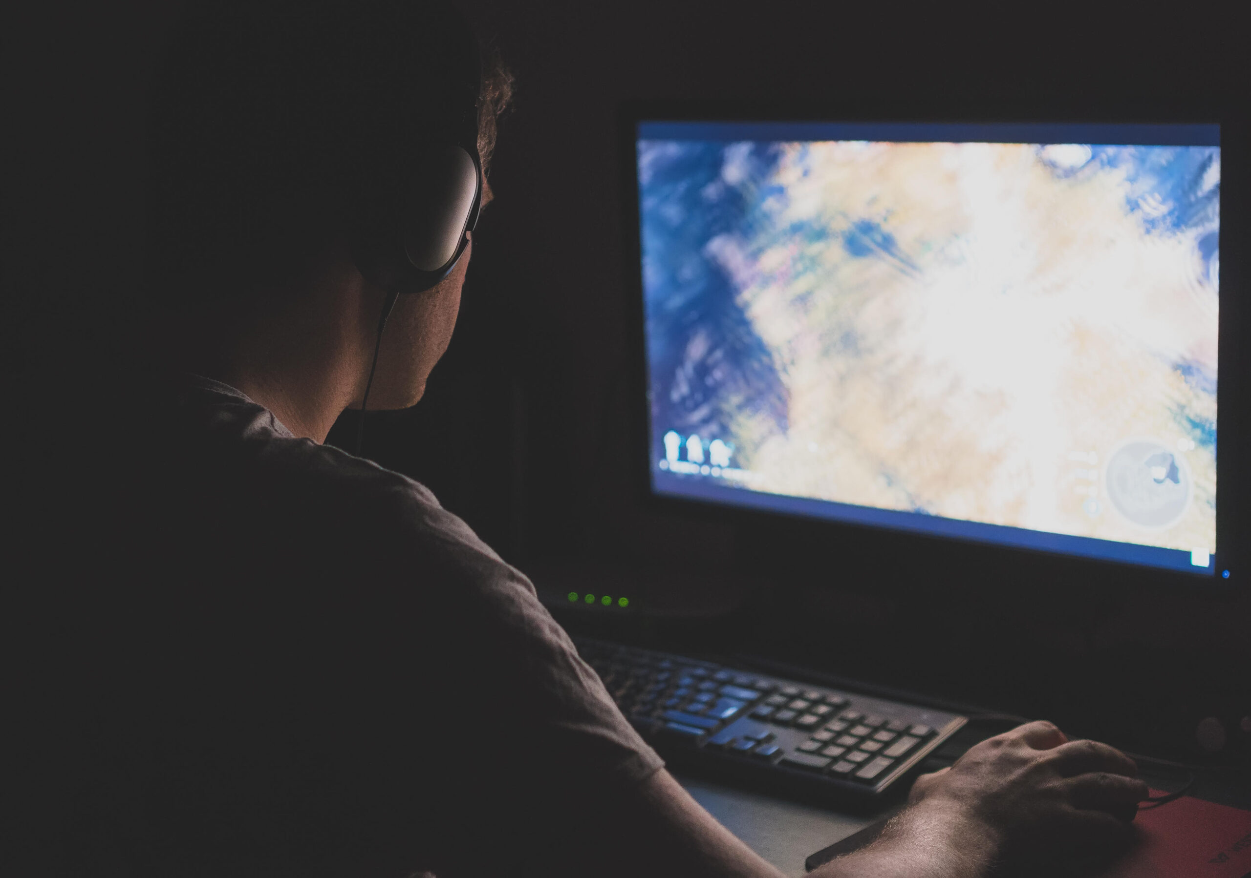 a man with headphones playing Mortal Shell 2 on his PC in a dark room